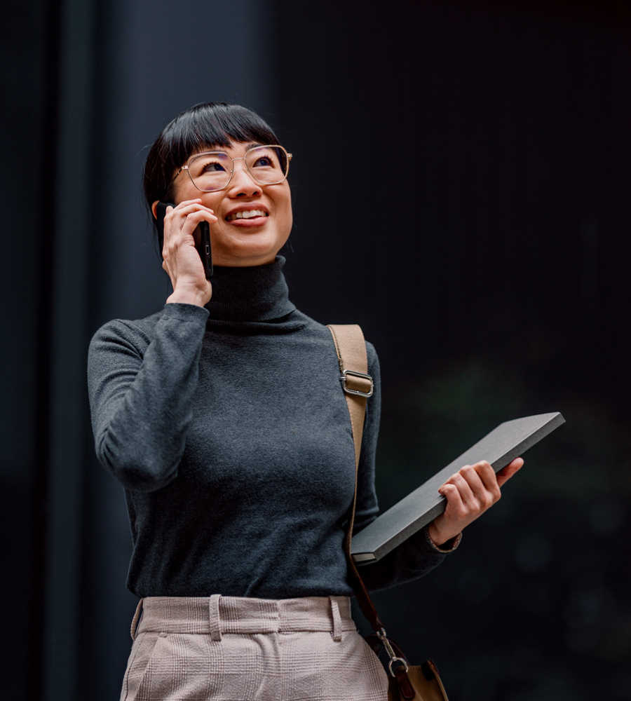 Anaplan Homepage Decision Excellence Image Woman holding a laptop while walking and smiling and talking on the phone