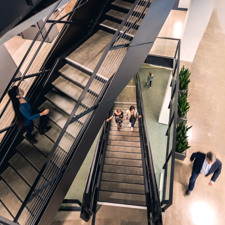 Contact Us Find Location Resource Tile Office workers using an stairs to move between floors, reflecting the dynamic nature of a bustling workplace.