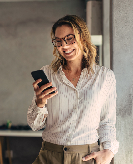 Supply Chain Solutions Overview Image A smiling woman wearing glasses holds her phone, radiating joy and engagement in a bright setting.